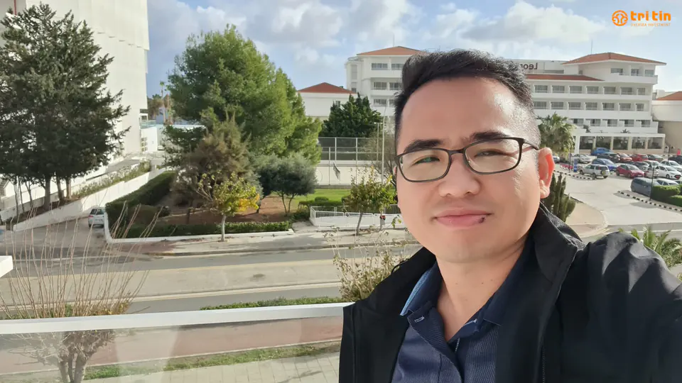 Đại diện Tri Tin trong chuyến thăm tại Síp, với cây xanh và các tòa nhà hoàn thiện phía sau
